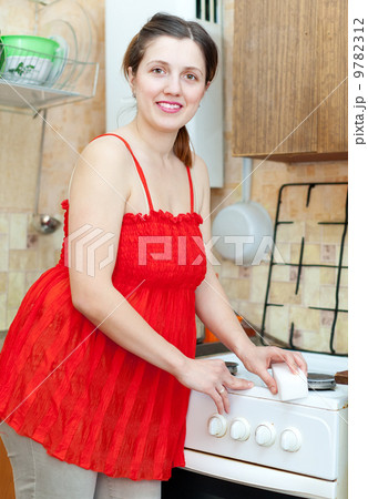 Happy woman in red cleans gas stove with sponge Happy woman in red cleans gas stove with sponge 9782312