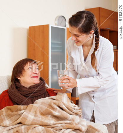 Smiling nurse in uniform caring for senior woman 9782370