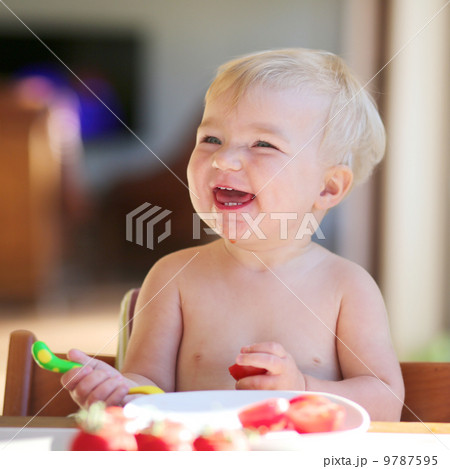 Funny happy healthy toddler sitting in high feeding chair eating cherry tomato 9787595