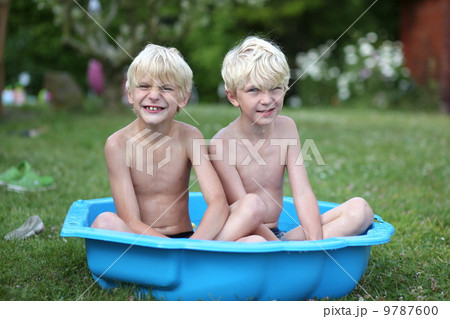Kids playing with water in little plastic bath outdoors in the garden at the backyard of the house 9787600