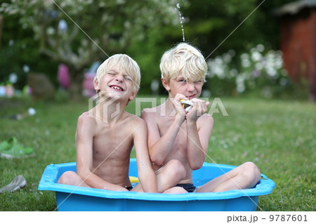 Kids playing with water in little plastic bath outdoors in the garden at the backyard of the house 9787601