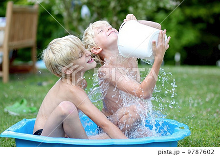 Kids playing with water in little plastic bath outdoors in the garden at the backyard of the house 9787602