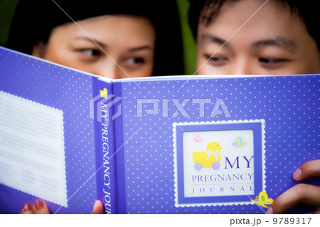 Asian pregnant couple reading a book together. Asian pregnant couple reading a book together. 9789317
