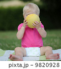 Adorable little girl is sitting on a carpet in a park and biting on a half of melon 9820928