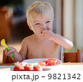 Funny happy healthy toddler sitting in high feeding chair eating cherry tomato 9821342
