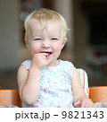 Funny happy healthy toddler sitting in high feeding chair biting on cherry tomato 9821343