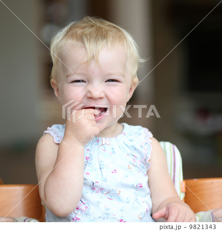 Funny happy healthy toddler sitting in high feeding chair biting on cherry tomato 9821343