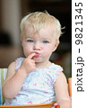Funny happy healthy toddler sitting in high feeding chair biting on cherry tomato 9821345