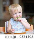 Cute baby girl sitting in a high feeding chair biting on delicious freshly cooked broccoli  9821508