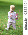 Adorable baby girl in beautiful kimono set is standing in a park with flowers in her hand  9822404