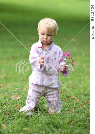 Adorable baby girl in beautiful kimono set is standing in a park with flowers in her hand  9822404