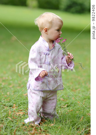 Adorable baby girl in beautiful kimono set is standing in a park with flowers in her hand  9822406