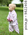 Adorable baby girl in beautiful kimono set is standing in a park with flowers in her hand  9822408