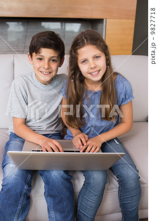 Portrait of young siblings using laptop in living room 9827718