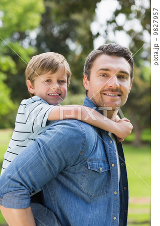 Portrait of father carrying boy on back at park 9827957