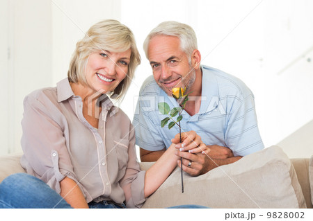 Man giving flower to a smiling woman sitting on couch Man giving flower to a smiling woman sitting on couch 9828002