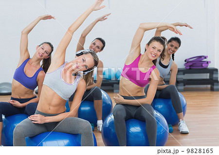 Sporty women stretching hands on exercise balls at gym Sporty women stretching hands on exercise balls at gym 9828165