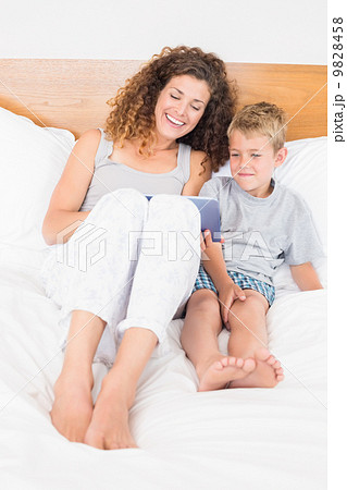 Happy mother and son sitting on bed with tablet pc Happy mother and son sitting on bed with tablet pc 9828458