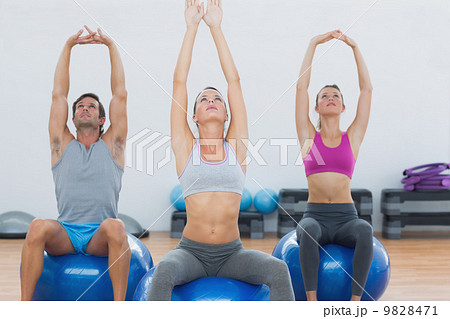 Sporty people stretching up hands on exercise balls at gym Sporty people stretching up hands on exercise balls at gym 9828471