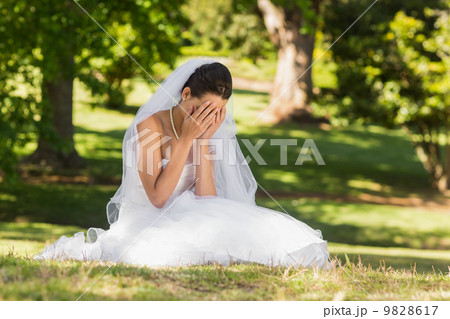 Beautiful worried bride sitting at park 9828617