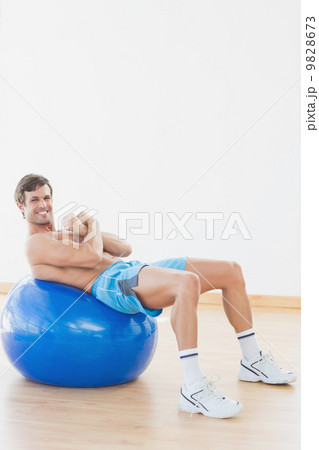 Shirtless man exercising on fitness ball in gym 9828673