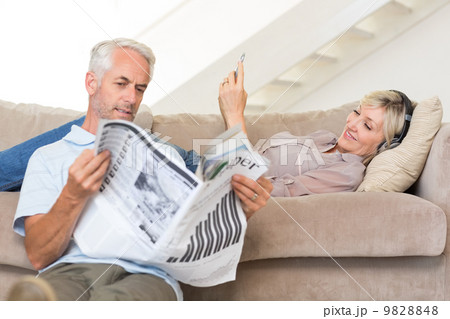 Couple with newspaper and cellphone in living room at home 9828848