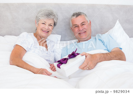 Senior man giving gift to wife in bed Senior man giving gift to wife in bed 9829034