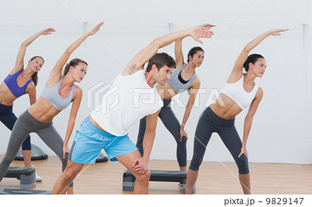 Class doing stretching exercise in fitness studio Class doing stretching exercise in fitness studio 9829147