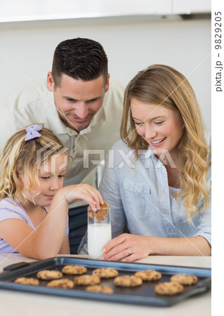 Parents looking at daughter dipping cookie in milk 9829205
