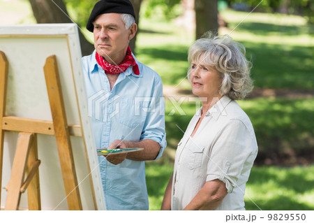 Woman watching mature man paint in park Woman watching mature man paint in park 9829550
