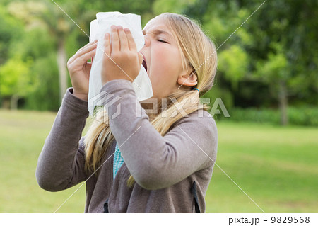 Girl sneezing into tissue paper at park Girl sneezing into tissue paper at park 9829568