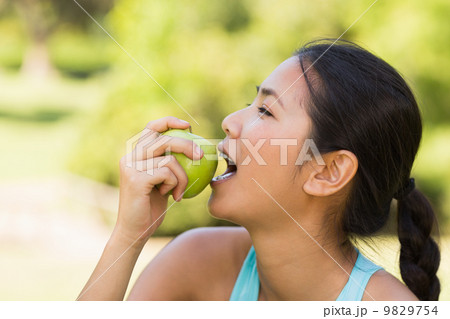 Healthy young woman eating apple in park 9829754