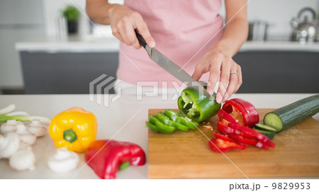 Mid section of a woman chopping vegetables in kitchen 9829953