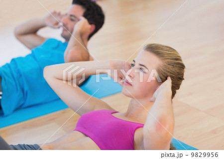 Side view of determined young couple doing sit ups Side view of determined young couple doing sit ups 9829956