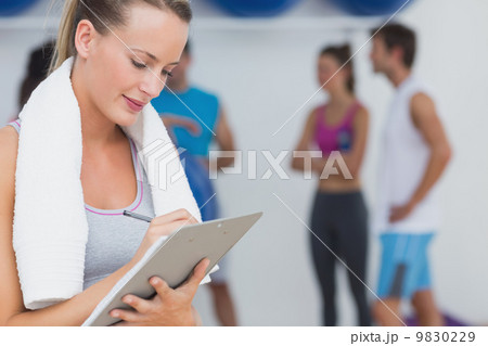 Trainer writing on clipboard with fitness class in background at Trainer writing on clipboard with fitness class in background at 9830229