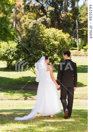 Rear view of newlywed couple walking in park 9830294