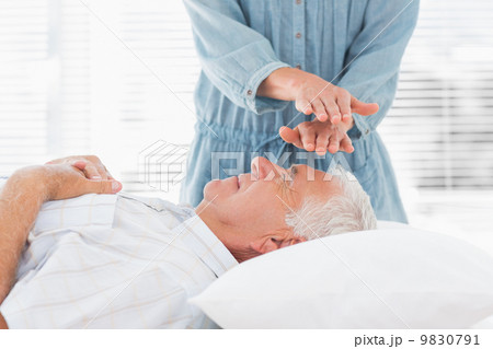 Massage therapist performing Reiki over man 9830791