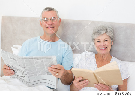 Senior couple holding newspaper and book in bed Senior couple holding newspaper and book in bed 9830936