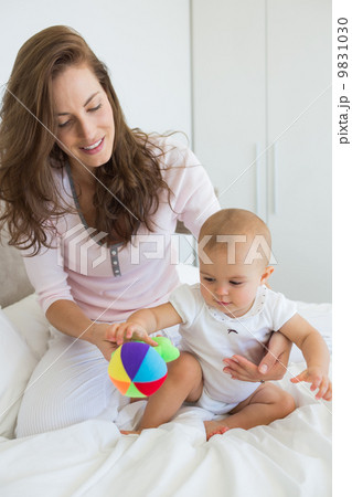 Mother and baby sitting with toy on bed Mother and baby sitting with toy on bed 9831030