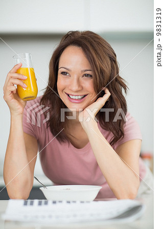 Woman with a bowl of cereals, orange juice and newspaper in kitc Woman with a bowl of cereals, orange juice and newspaper in kitc 9831319