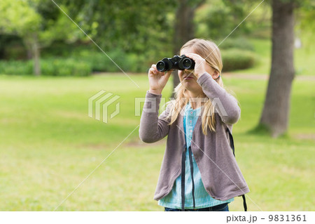 Young girl looking through binoculars at park 9831361