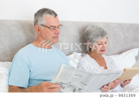 Senior couple with newspaper and book in house 9831369