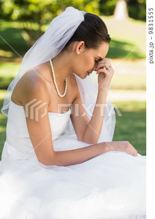 Beautiful worried bride sitting at park 9831555