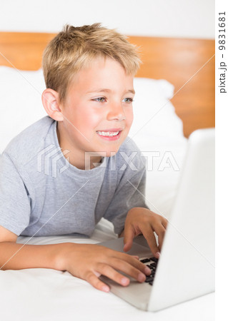 Blonde boy lying on bed using laptop 9831681