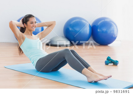Smiling woman doing sit ups in fitness studio Smiling woman doing sit ups in fitness studio 9831691