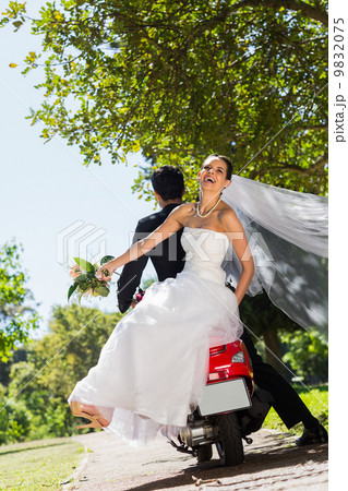 Newlywed couple sitting on scooter in park 9832075