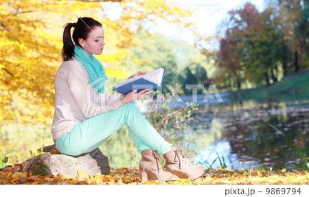 Young girl relaxing in autumnal park reading book 9869794