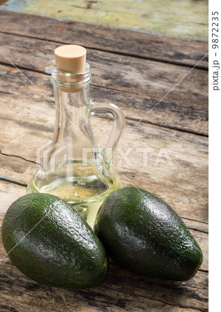 Two Raw Avocado with Bottle of Oil on Grunge Wood Background 9872235