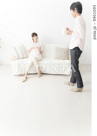 コーヒーを運ぶ女性とソファに座りタブレットを操作する男性 9901095