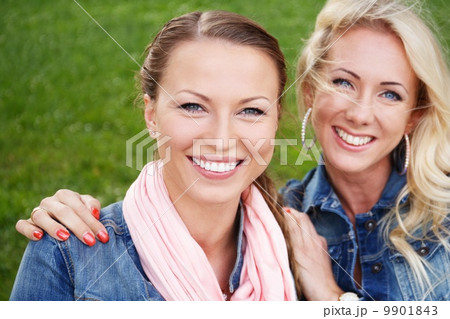 Two beautiful smiling young women in jeans jackets sitting on a bench in a park Two beautiful smiling young women in jeans jackets sitting on a bench in a park 9901843